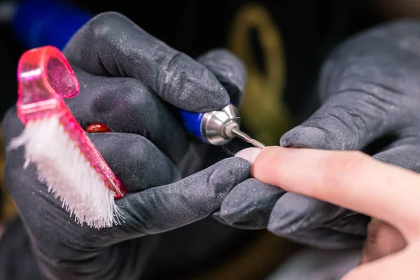 Маникюрша использует электрическую дрель для ногтей в салоне красоты. Идеальный процесс маникюра ногтей близко с разрывом летающих обломков. — стоковое фото