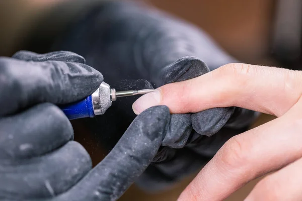 Manicurista utilizar taladro lima de uñas eléctrica en el salón de belleza. Perfecto proceso de manicura uñas de cerca con ráfaga de escombros voladores. — Foto de Stock