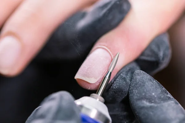 Woman use electric nail file drill in beauty salon. Nails manicure process in detail. Gel polish close-up concept.