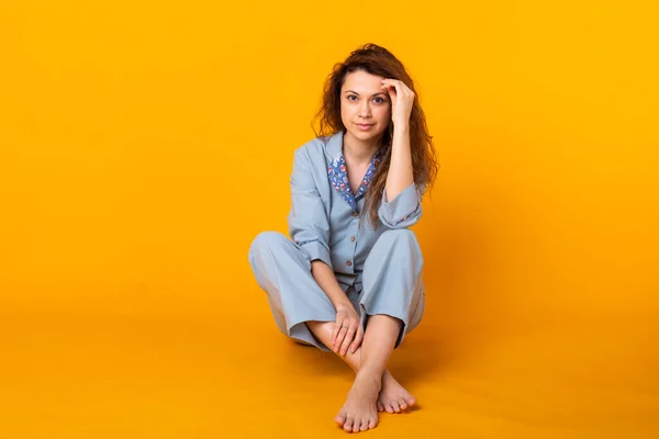 Närbild ung kvinna i blå hemkläder. Isolerad på gul bakgrund. Pajama-konceptet. — Stockfoto