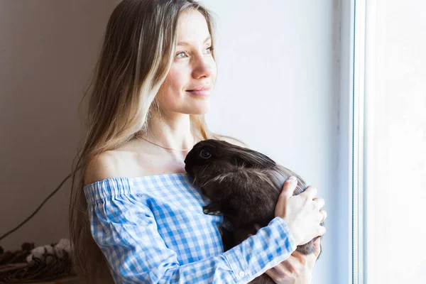 Huisdier en Pasen concept - Gelukkig meisje knuffelen bruin konijn thuis. — Stockfoto