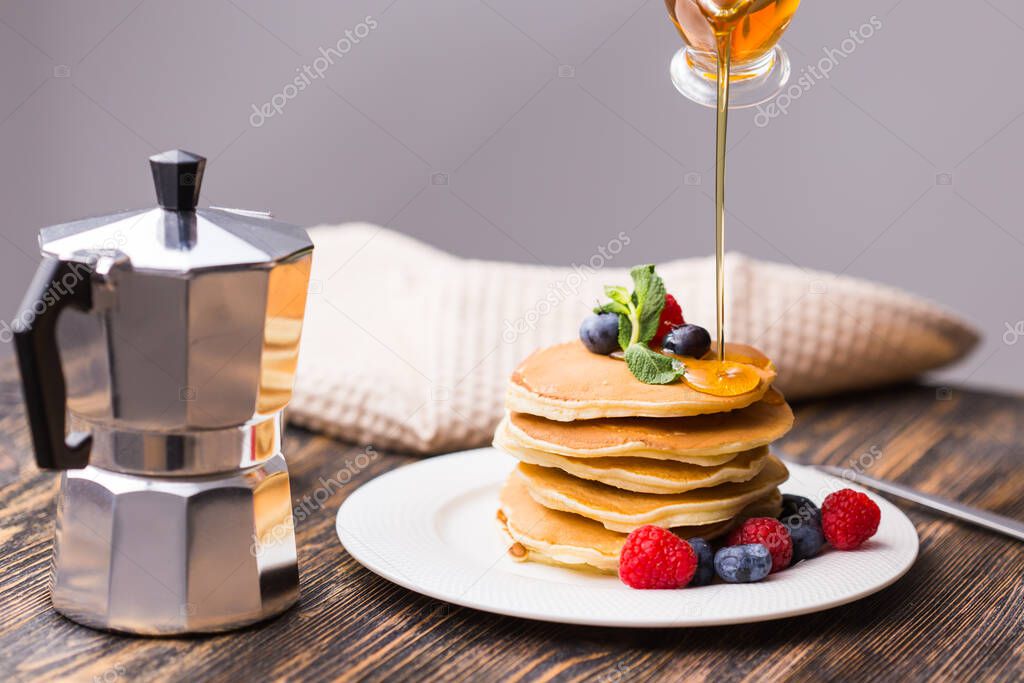 Woman pouring maple syrup on tasty pancakes.