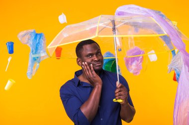 Çöp, plastik geri dönüşüm, çevre kirliliği ve ciddi bir Afro-Amerikan erkeği sarı arka planda çöp arıyor. Ekoloji hakkında düşünüyor.