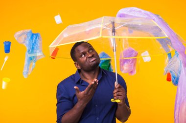 Çöp, plastik geri dönüşüm, çevre kirliliği ve ciddi bir Afro-Amerikan erkeği sarı arka planda çöp arıyor. Ekoloji hakkında düşünüyor.