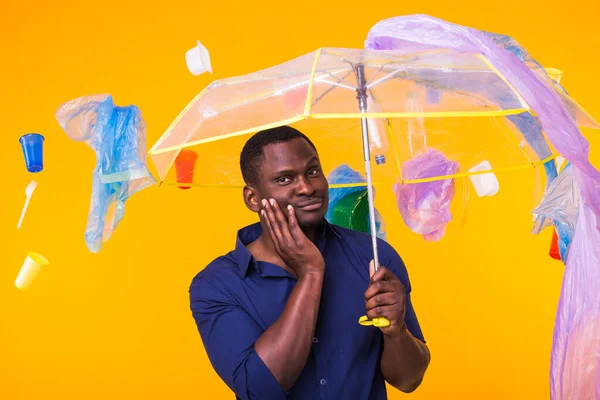 Çöp, plastik geri dönüşüm, çevre kirliliği ve ciddi bir Afro-Amerikan erkeği sarı arka planda çöp arıyor. Ekoloji hakkında düşünüyor.