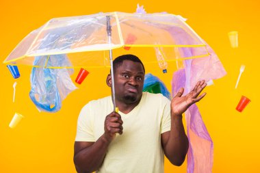 Çöp, plastik geri dönüşüm, kirlilik ve çevre konsepti sorunu - sarı arka planda çöplü dalgın Afrikalı Amerikalı adam.