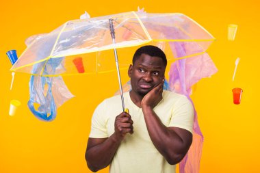Çöp, plastik geri dönüşüm, kirlilik ve çevre konsepti sorunu - sarı arka planda çöplü dalgın Afrikalı Amerikalı adam.