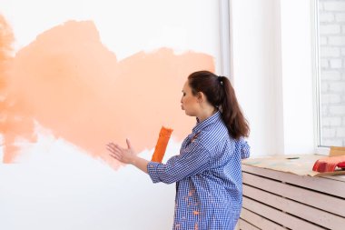 Duvarı boya silindiriyle boyayan komik bir kadın. Yeni dairesinde duvar boyayan güzel bir kadının portresi. Dekorasyon ve yenileme konsepti.