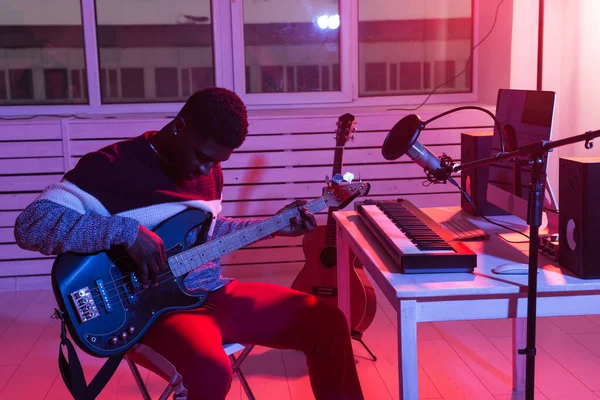 Create music and a recording studio concept - african american man guitarist recording electric bass guitar track in home studio