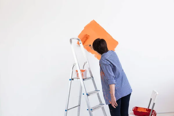 Apartmanda tamirat var. Mutlu orta yaşlı kadın duvarı boyuyor.. — Stok fotoğraf