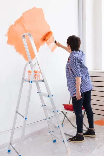 Riparazione nell'appartamento. Felice donna di mezza età dipinge il muro con vernice. — Foto Stock