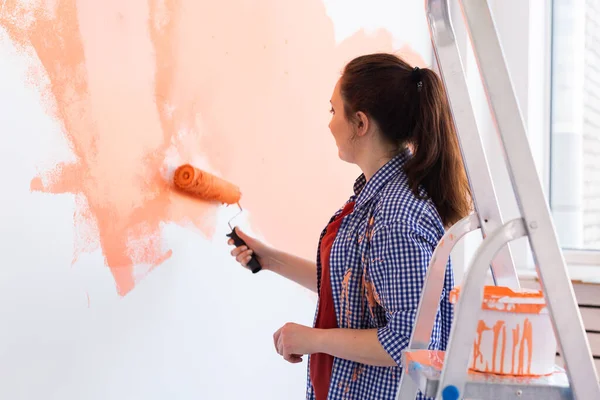 stock image Pretty smiling woman painting interior wall of home with paint roller. Redecoration, renovation, apartment repair and refreshment concept.