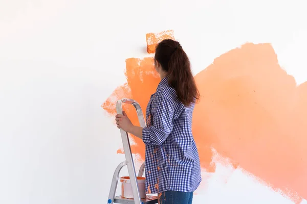 Felice giovane donna pittura parete interna con rullo di vernice in nuova casa. Una donna con rullo che applica vernice su un muro . — Foto Stock