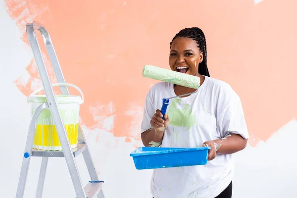 Sorridente donna afroamericana pittura parete interna della casa. Concetto di ristrutturazione, riparazione e ridecorazione. — Foto Stock