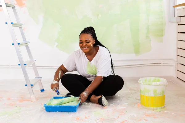 Güzel gülümseyen Afro-Amerikan kadın evin içini boya rulosuyla boyuyor. Dekorasyon, yenileme, apartman onarımı ve ferahlatıcı konsept. — Stok fotoğraf
