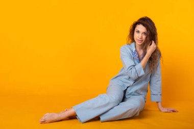 Pijamalı gülümseyen genç kız, sarı arka plan stüdyo resminde dinlenirken poz veriyor. Rahatla iyi ruh hali yaşam tarzı konsepti.