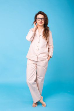 Pijamalı gülümseyen genç kız, mavi arka plan stüdyo resmine izole edilmiş evde dinlenirken poz veriyor. Rahatla iyi ruh hali yaşam tarzı konsepti.