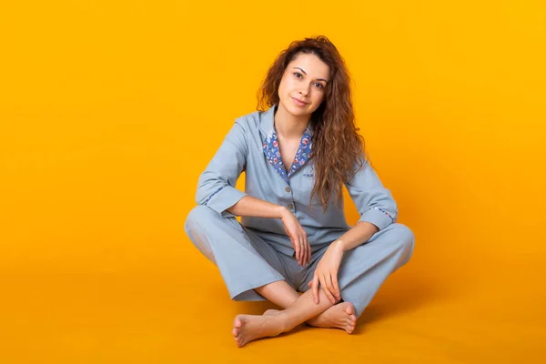 Chica joven sonriente en pijama ropa de casa posando mientras descansa en casa aislado en retrato de estudio de fondo amarillo. Relajarse concepto de buen humor estilo de vida . — Foto de Stock