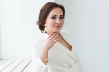 Beyaz elbiseli, makyajlı, beyaz bir odada poz veren bir kız. Moda stili stüdyo boy portresi. Zarif, zarif bir kadın..