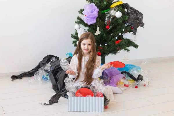 Protección del medio ambiente y concepto de contaminación. Triste caja de transporte infantil con basura de plástico sobre el fondo del árbol de Navidad . — Foto de Stock