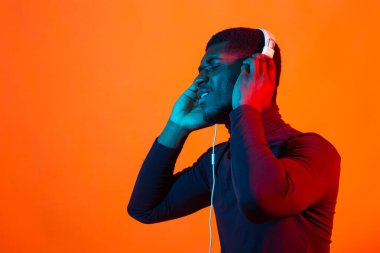 Genç Afro-Amerikalı adamlar, neon ışıkta kulaklıkla müzik dinliyorlar. Erkek portresi. İnsan duyguları kavramı, yüz ifadesi, tatiller veya hafta sonları, hobi,