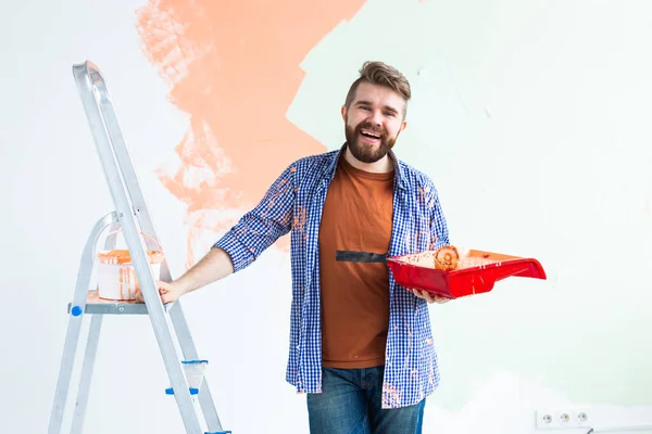 Man painting the wall with paint roller. Portrait of a guy painting wall in her new apartment. Redecoration and renovation concept. — Stock Photo, Image