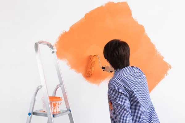 Glad medelålders kvinna målning interiör vägg med färg roller i nytt hus. En kvinna med roller applicera färg på en vägg. — Stockfoto