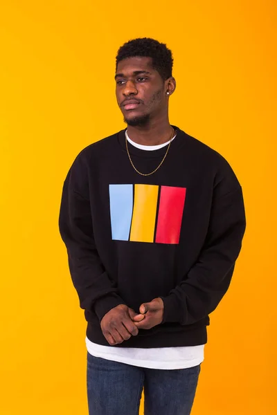 Portrait handsome young black man dressed in jeans and sweatshirt on yellow background. Street fashion and modern youth culture. — Stock Photo, Image