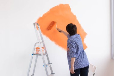 Gülümseyen orta yaşlı kadın evin içini boyuyor. Yenileme, onarım ve yeniden dekorasyon konsepti.