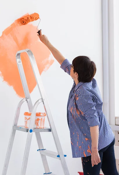 Hermosa mujer de mediana edad pintando la pared con rodillo de pintura. Retrato de una joven mujer hermosa pintando la pared en su nuevo apartamento. Concepto de reacondicionamiento y renovación. — Foto de Stock