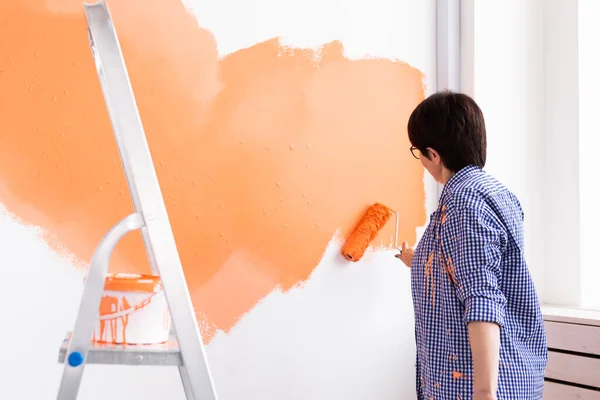 Hermosa mujer de mediana edad pintando la pared en su nuevo apartamento. Concepto de renovación y redecoración. — Foto de Stock