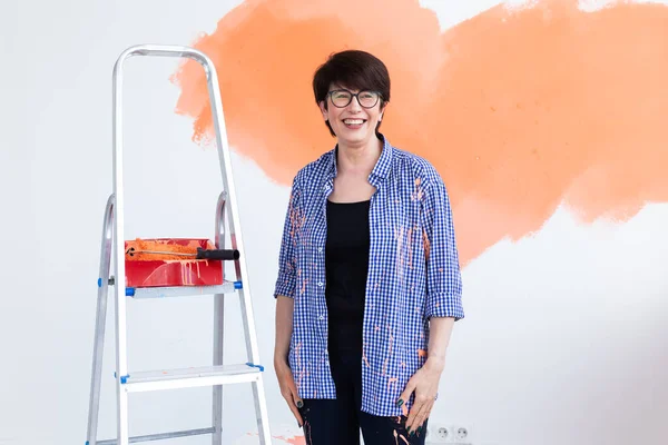 Gelukkige vrouw van middelbare leeftijd die muren schildert in haar nieuwe appartement. Renovatie, herinrichting en reparatie concept. — Stockfoto