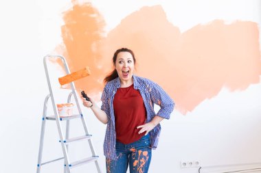Yeni dairesinde dans eden komik, genç bir kadın duvar boyuyor. Yenileme, dekorasyon ve onarım konsepti.