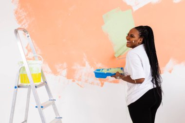 Mutlu gülümseyen Afrikalı Amerikalı kadın yeni evin iç duvarını boyuyor. Dekorasyon, yenileme, apartman onarımı ve ferahlatıcı konsept.