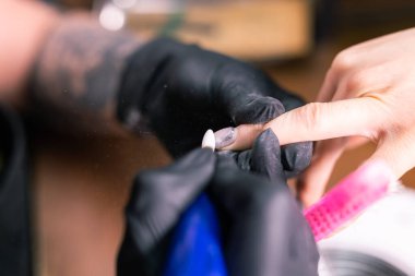 Kadın usta kuaförde manikür yaparken ojeyi çıkarmak için elektrikli makine kullanıyor. Yakın çekim donanım manikürü. El bakımı kavramı. Kadın manikürcü, bir değirmen kesicisiyle tırnaklarını temizliyor.