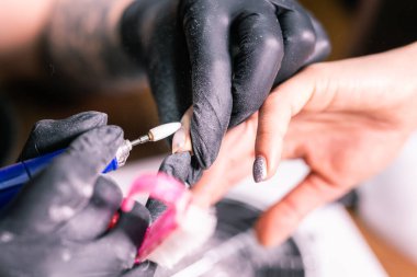 Manikürcü kadının yakın çekimi, manikür makinesi kullanarak müşterilerin tırnaklarındaki jöle parlatmasını kaldırıyor. Manikür ustası güzellik salonunda elektrikli tırnak matkabıyla çalışıyor. Donanım manikür süreci.