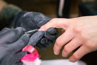 Kadın güzellik salonunda elektrikli tırnak matkabı kullanıyor. Manikür işlemini detaylıca yapıyor. Jel cilası kavramı.