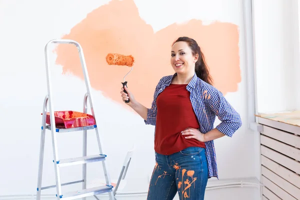 Hermosa mujer pintando la pared en su nuevo apartamento. Concepto de renovación y redecoración. — Foto de Stock