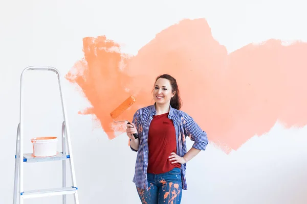Beautiful female painting the wall with paint roller. Portrait of a young beautiful woman painting wall in her new apartment. Redecoration and renovation concept. — Stock Photo, Image