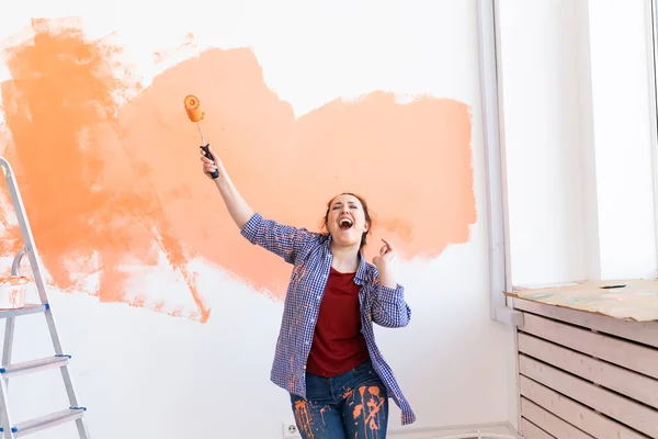 Ballando divertente pittura femminile la parete con rullo di vernice. Ritratto di una giovane bella donna che dipinge un muro nel suo nuovo appartamento. Concetto di ristrutturazione e riqualificazione. — Foto Stock