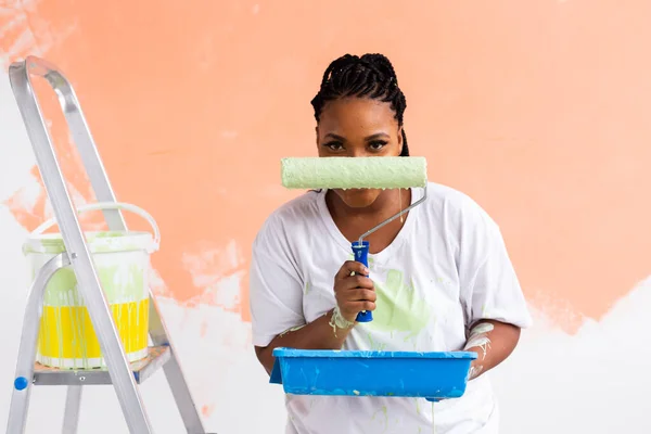 Mutlu gülümseyen Afrikalı Amerikalı kadın yeni evin iç duvarını boyuyor. Dekorasyon, yenileme, apartman onarımı ve ferahlatıcı konsept. — Stok fotoğraf