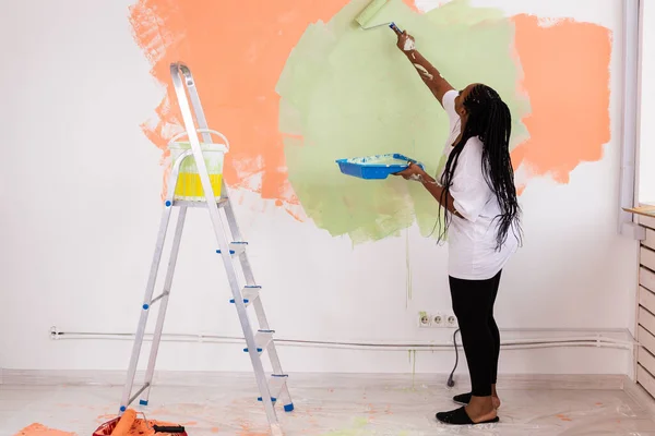 Usmívající se Afroameričanka maluje vnitřní stěnu domova. Koncepce rekonstrukce, opravy a rekonstrukce. — Stock fotografie