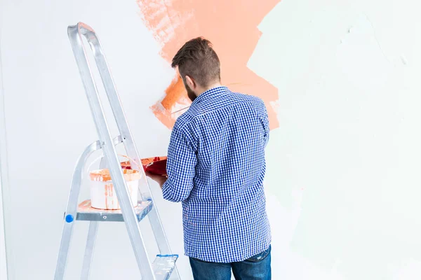 Hombre pintando la pared interior del hogar con rodillo de pintura. Redecoración, renovación, reparación de apartamentos y concepto de refresco. Vista trasera . — Foto de Stock