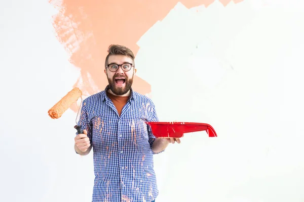 Funny man painting interior wall of home with paint roller. Redecoration, renovation, apartment repair and refreshment concept. — Stock Photo, Image