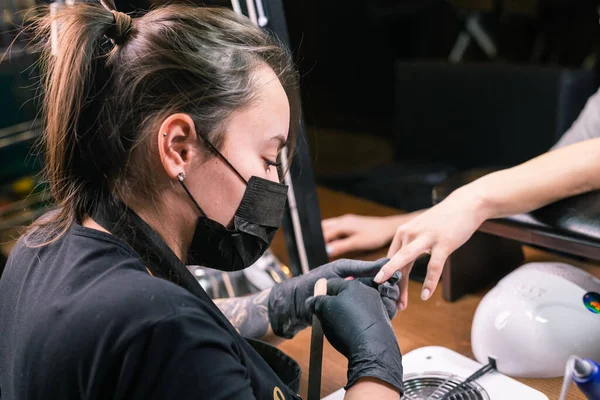 Female master uses an electric machine to remove the nail polish during manicure in the salon. Close-up hardware manicure. Concept of hand care. Female manicurist cleaning of nails by a milling cutter