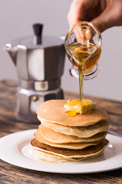 Close-up of pouring maple syrup on stack of pancakes.