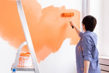 Yenileme, dekorasyon ve onarım konsepti - orta yaşlı kadın yeni evinde duvar boyuyor.