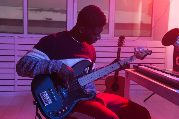 Create music and a recording studio concept - African american man guitarist recording electric bass guitar track in home studio
