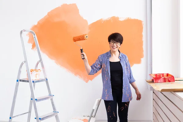 Beautiful middle-aged female painting the wall with paint roller. Portrait of a young beautiful woman painting wall in her new apartment. Redecoration and renovation concept. — Stock Photo, Image
