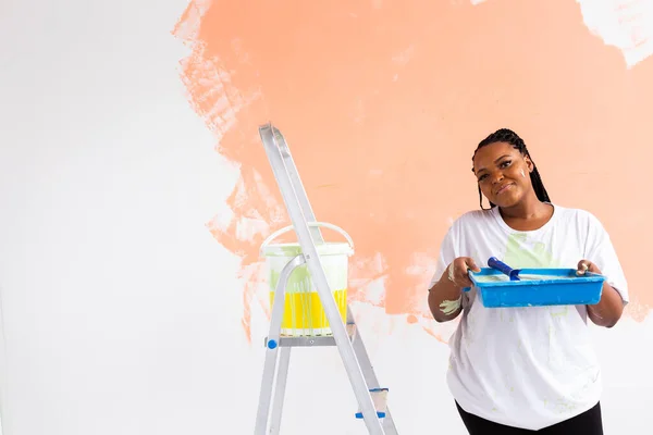 Donna afro dipingere le pareti della nuova casa. Concetto di ristrutturazione, riparazione e ridecorazione. — Foto Stock